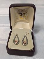 Teardrop shaped silver earrings each featuring a gold heart inside, displayed in a burgundy jewelry box.