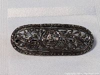 Close-up photo showing front face of the oval sterling silver antique pin brooch with floral filigree and marcasite stones.