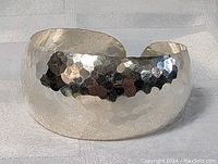 Close-up front view of wide sterling silver hammered cuff bracelet lying on fabric surface.