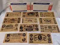 Photo showing two labeled cardboard holders with multiple Confederate currency notes laid out in front. The notes include various denominations and states, well preserved and in excellent condition.
