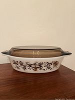 Side view of the Pyrex casserole dish with Brown Vine pattern and smoked glass lid, showing one handle and floral decorations.
