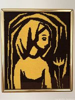 Front view of the framed vintage needlepoint art showing a stylized female figure in gold and brown against a dark background.