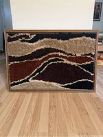 Front view of one large framed vintage 1970s rug art piece with multicolor textured shag pattern in abstract design, wood frame, placed on wood floor.