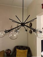 Side angled view showing dark brown metal arms and clear droplet-shaped glass around bulbs, hanging over seating area.