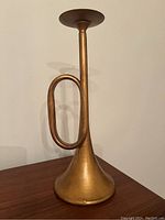 Photo of the trumpet-shaped candle holder showing its copper/gold tone metal surface and design from a side angle on a wooden surface.
