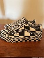 Side view showing the Vans women's checkerboard sneakers with full black and white checkerboard pattern across the canvas and midsole. Heel 'Off the Wall' tag visible.