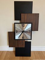 Full view of the vintage Caravelle wall clock showing the vertical arrangement of five rectangular panels with alternating faux wood and black finishes, and square metallic clock face in center.