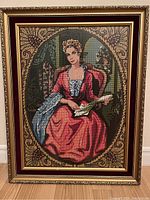 Full view of vintage needlepoint artwork with ornate gold frame and burgundy velvet border on white wall.