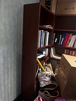 Side view of one dark wooden bookcase filled with various books and binders, some items on lower shelves and floor not included.
