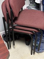 Four stackable office chairs pictured stacked together, showing black metal frames and burgundy fabric seats and backs.