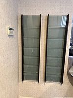 Two tall dark wooden magazine racks with glass panels leaning against a wall