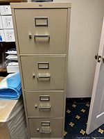 Front view of the 4 drawer beige metal filing cabinet showing each drawer with handles and label holders.