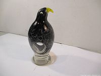 Front view of the black and white art glass bird figurine with yellow beak on a clear base with hollow center.