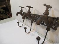 Side angled view of set of three cast iron wall hooks designed like faucets, showing detail of spout, handle and ball tip hook.