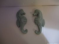 Front view of two green chalkware seahorse figures placed side by side against a white background, showing texture and details of fins and ridges.