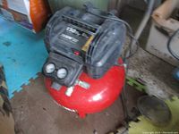 Full view of air compressor showing red tank and black motor housing with gauges and fittings on top.