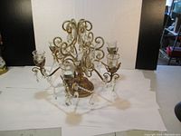 Front view of ornate crystal candle centerpiece showing five glass candle holders and intricate gold-toned metal design with hanging crystal prisms.