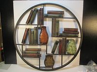 Full front view of round metal wall art with shelves containing metal books and vases