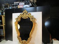 Front view of ornate gold-tone faux wood framed mirror placed against a dark background.