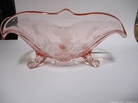 Frontal view of the pink translucent glass bowl showing the curved scalloped edge and three legs.