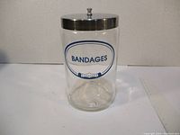 Clear glass jar with metal lid and blue and white label reading 'Bandages Profex'