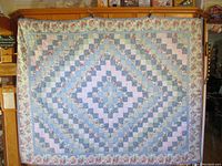 Full view of patchwork quilt hanging showing diamond pattern made from small squares in pastel colors and floral prints with floral border.