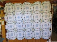 Full view of the white quilt displayed on a wooden backdrop showing full pattern of double wedding rings and stars.