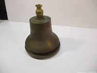 Side view of the solid brass bell showing overall shape and brass pineapple finial on top.