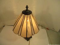 Photo of the translucent cream and amber stained glass shade with metal leading, showing the lamp's top and the warm glow from the internal bulb.