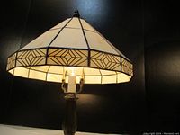 Lamp illuminated to show light diffusion through stained glass shade with geometric arrowhead border pattern.