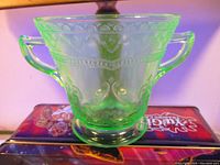 Front view showing the etched decorative pattern on the uranium glass sugar bowl and its two handles.
