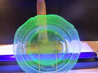 Top view of the uranium glass plate illuminated under UV light showing bright green fluorescence and decorative pattern.