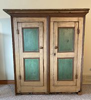Front view of armoire showing two cream-painted doors with green inset panels.