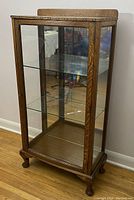 Angled front-left view showing oak frame, decorative trim, glass shelves, and mirrored back.