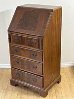 Front angled view of antique solid wood secretary desk with closed slant front and four drawers.