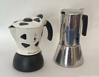 Both coffee makers side by side, showing the stainless steel coffee maker and the cow print Mukka Express in good condition.