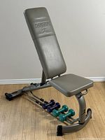 View of the Danskin adjustable weight bench with gray padded surfaces and metal frame, showing the bench in near upright position with dumbbells placed on the rack below.
