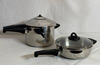 Both stainless steel items shown together, pressure cooker and saucepan with glass lid, black handles visible
