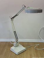 Full side view of the large magnifying floor lamp showing white finish, adjustable arm with springs, heavy metal base, and power cord.