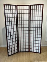 Full view of the three-panel privacy screen standing upright, showing dark wood grid frame and white paper backing with slight damages.