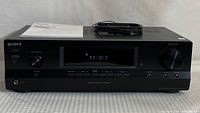 Front view of Sony STR-DH130 stereo receiver showing digital display, input selector, volume knob, headphone jack, and control buttons with user manual and remote on top