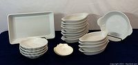 Full lot overview showing multiple small oval dishes stacked, scallop-shaped plates, shell-shaped plates, and the large rectangular baking dish