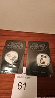 Two 2011 Star Wars collector coins sealed in packaging, displayed on a wood surface. Coins feature portraits of Luke Skywalker and Princess Leia.