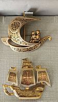 Photo shows two vintage brooches: one a crescent moon with a couple inside, one a sailing ship with three sails, all gold-tone metal with engraved patterns.