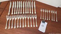 Full set arranged on wood surface with 12 knives, 12 forks, and 8 smaller forks.