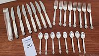 Full set of 24 pieces laid out on wood surface: 8 knives, 8 forks, 8 spoons.