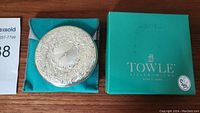 Silver embossed compact mirror with ornate design on turquoise pouch and green Towle Silversmiths box with logo.
