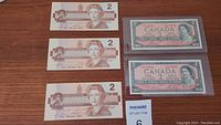 Six Canadian 2 dollar bills in two different designs neatly laid out, showing front sides with Queen Elizabeth II.
