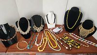 Full view of the lot showing various vintage necklaces laid on a wood surface and displayed on necklace busts.