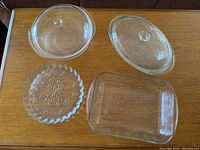 Top-down view of all four clear glass vintage baking dishes on a wooden surface showing lids and open dishes.